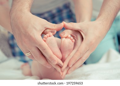 Mother And Father Hold Feet Of Newborn Baby