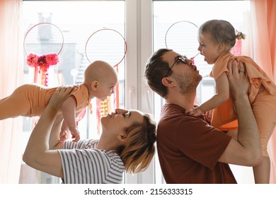 Mother and father holding children in the air over decorated with Dreamcatchers sunny window at home. Happy parents playing with infant, toddler on sunlight. Positive future motherhood, parenthood - Powered by Shutterstock