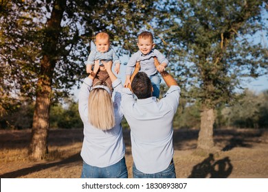 Mother And Father Holding Up Their Two Sons And. Family Of Four Dressed In The Same Style And Color Clothes. Focus On The Parents.