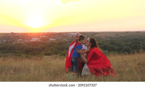 Mother And Father Kiss And Hug Little Child Sunset, Playing Superheroes Dressed Red Cloaks, Happy Family, Brave Savior Costume, Fantastic Childhood Dream Heroes, Fearless Kid Boy Winner Fun Play Game