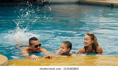 The Mother And Father With Little Daughter Have Fun In The Pool. Mom And Dad Plays With The Child. The Family Enjoy Summer Vacation In A Swimming Pool Jumping, Spinning, Splash Water. Slow Motion.