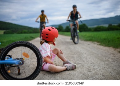 Mother And Father Rushing To Help Their Little Daughter After Falling Off Bicycle Outdoors