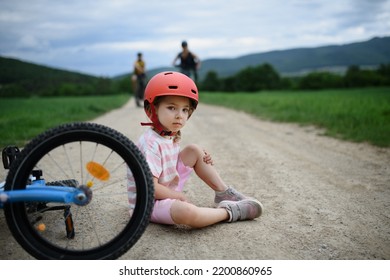 Mother And Father Rushing To Help Their Little Daughter After Falling Off Bicycle Outdoors