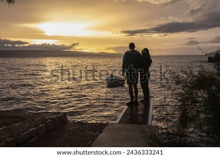 Mother and father with small child enjoying romantic sunset at small pier at Punta Rata beach in idyllic town Brela, Makarska Riviera, Dalmatia, Croatia. Dreamlike atmosphere. Family vacation concept