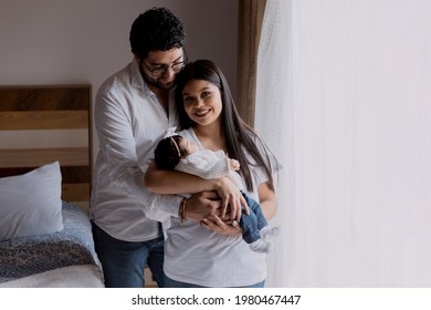 Mother And Father Smiling While Holding Their Newborn Baby In Their Arms - Happy Young Hispanic Parents With Their Newborn Baby