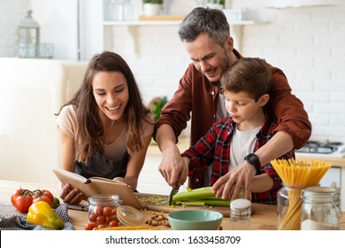 Mother, Father, Son Chopping Vegetables On Kitchen. Salad Preparation For Dinner Or Lunch. Father Helping Boy Child Chopping Celery. Toothy Smiling Mother Telling Recipe From Cookbook. Happy Family