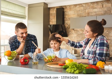 Mother Father And Son At Home Standing Leaning On Table In Kitchen Together Parents Looking At Boy Mixing Salad With Wooden Spoon Smiling Proud Mom Touching His Head Cheerful.