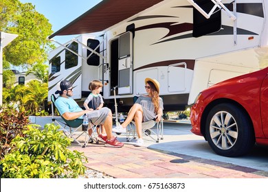 Mother, Father And Son Sitting Near Camping Trailer,smiling.Woman, Men, Kid Relaxing On Chairs Near Car And Palms.Family Spending Time Together On Vacation Near Sea Or Ocean In Modern Rv Park