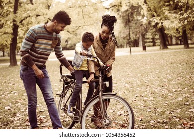 Mother And Father Teaching Their Daughter To Drive Bike.