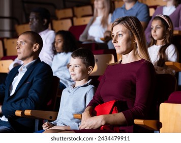 mother, father and their children sitting at perfomance in theatrical auditorium
