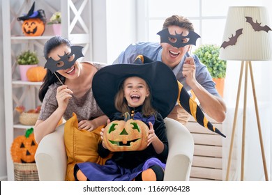 Mother, Father And Their Kid Having Fun At Home. Happy Family Celebrating Halloween. Child Wearing Carnival Costume.