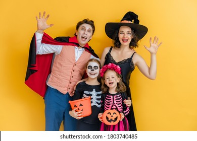 Mother, Father And Their Kids Having Fun At Party. Happy Family Celebrating Halloween. People Wearing Carnival Costumes And Makeup On Yellow Wall Background.