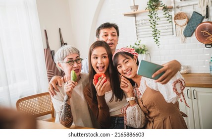 Mother And Father And Two Daughter Cooking In Kitchen, Using Smart Phone To Take Selfies, Happy Family.