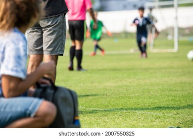 Mother And Father Watching Their Son Playing Football In A School Tournament On A Clear Sky And Sunny Day. Sport, Active Lifestyle, Happy Family And Soccer Mom, Soccer Dad Concept.