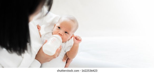 Mother Feeding Asian Baby With Bottle Of Milk, Banner Copy Space