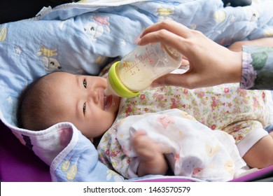 Mother Feeding Baby From Bottle. Cute And Smiling Asian Baby Drinking Milk From Bottle While Lying On Baby Carriage With Blanket.