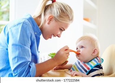 Mother Feeding Baby Boy In High Chair