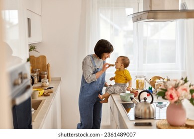 Mother feeding baby boy in the kitchen - Powered by Shutterstock