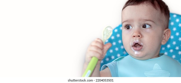 Mother Feeding Baby Boy With Mashed Food Puree Yogurt Healthy Diversification.toddler In High Chair Side View Green Silicone Spoon.wide Open Mouth Hungry Boy.wide Banner Child With Spoon In Hand.dirty