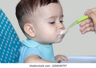 Mother Feeding Baby Boy With Mashed Food Puree Yogurt Healthy Diversification.toddler In High Chair Side View Green Silicone Spoon.wide Open Mouth Hungry Boy.wide Banner Child With Spoon In Hand.dirty