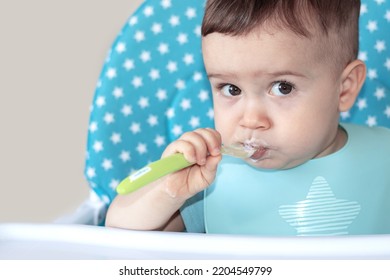 Mother Feeding Baby Boy With Mashed Food Puree Yogurt Healthy Diversification.toddler In High Chair Side View Green Silicone Spoon.wide Open Mouth Hungry Boy.wide Banner Child With Spoon In Hand.dirty