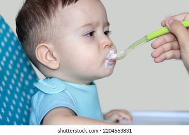 Mother Feeding Baby Boy With Mashed Food Puree Yogurt Healthy Diversification.toddler In High Chair Side View Green Silicone Spoon.wide Open Mouth Hungry Boy.wide Banner Child With Spoon In Hand.dirty