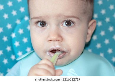 Mother Feeding Baby Boy With Mashed Food Puree Yogurt Healthy Diversification.toddler In High Chair Front View Chewing Green Silicone Spoon.wide Open Mouth Hungry Boy.adorable Cute Boy