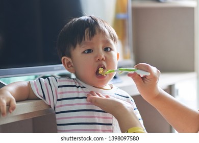 Mother Feeding Cute Asian Baby With Porridge.