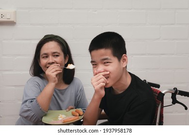 Mother Feeding Food To Disabled Child On The Wheelchair In Home By Love Her Son, Daily Routine Of Special Need Children's, Lifestyle In Kids Is Difficult To Eat, Care For Disability Person Concept.