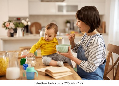 Mother feeding her baby boy with corn flakes at the table at home - Powered by Shutterstock