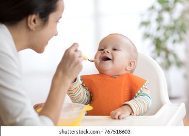 Mother feeding her baby son with spoon. Mother giving healthy food to her adorable child at home - Powered by Shutterstock