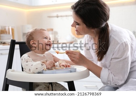 Mother feeding her cute little baby in kitchen