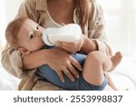 Mother feeding her little baby from bottle on bed indoors, closeup