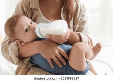 Mother feeding her little baby from bottle on bed indoors, closeup - Powered by Shutterstock