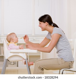 Mother feeding hungry baby in highchair in kitchen - Powered by Shutterstock