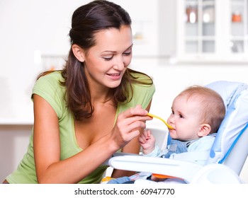 Mother feeding hungry baby in the highchair indoors - Powered by Shutterstock