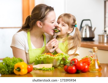 Mother Feeding Kid Vegetables In Kitchen