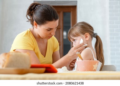 Mother Feeds Her Daughter With Food From Spoon And Wipes Her Face With Napkin. Maternal Care Of Child Kid Girl Real Lifestyle Lunch Of Disgruntled Kids