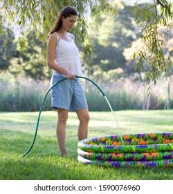 Mother Filling A Paddling Pool With A Garden Hose