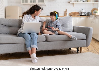 Mother freelancer enjoy helping little son with homework and distance lessons while working remotely on freelance project from home during corona virus epidemic lockdown. Mom and kid learning together - Shutterstock ID 1994264786