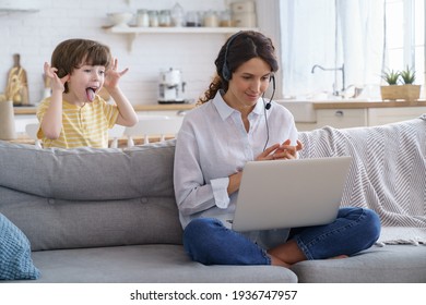 Mother freelancer talking on video call, remote working on laptop from home office with kid during lockdown. Children make noise disturb woman at work, shows tongue standing behind couch. Distance job