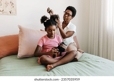 Mother gently combing her daughter's Afro hair, styling it into two neat buns. Black mom caring for her young child's coily hair, which is an important part of black women's cultural heritage. - Powered by Shutterstock