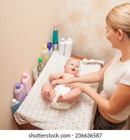 Mother Getting Dressed Her Baby On The Changing Diaper Table