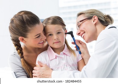 Mother with girl being examined by female doctor with otoscope in clinic