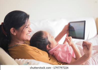 Mother With Girl Child In Bed Playing Games On Tablet