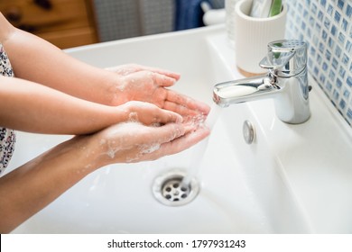 Mother And Girl Child Washing Hands Together In Bathroom Sink With Soap Under Running Water Tap To Rinse Off. Fingers Hands Extended Open. High Point Of View