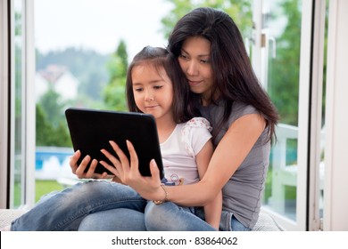 Mother and girl holding E-book reader at home