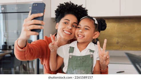 Mother, girl and phone selfie while cooking in kitchen, bonding and having fun. Learning, baking and mom, kid and 5g mobile for social media, picture or online post with victory hands or peace sign - Powered by Shutterstock