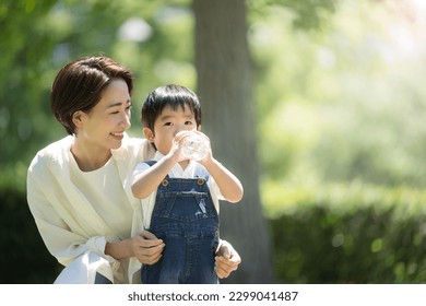 A mother gives her child a drink of water in a fresh green park. An image of hydration in the hot sun in summer. Copy space is available on the right. - Powered by Shutterstock