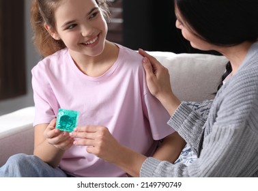 Mother giving condom to her teenage daughter at home.